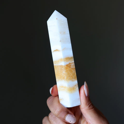 Hand holding a striped calcite crystal against a dark background