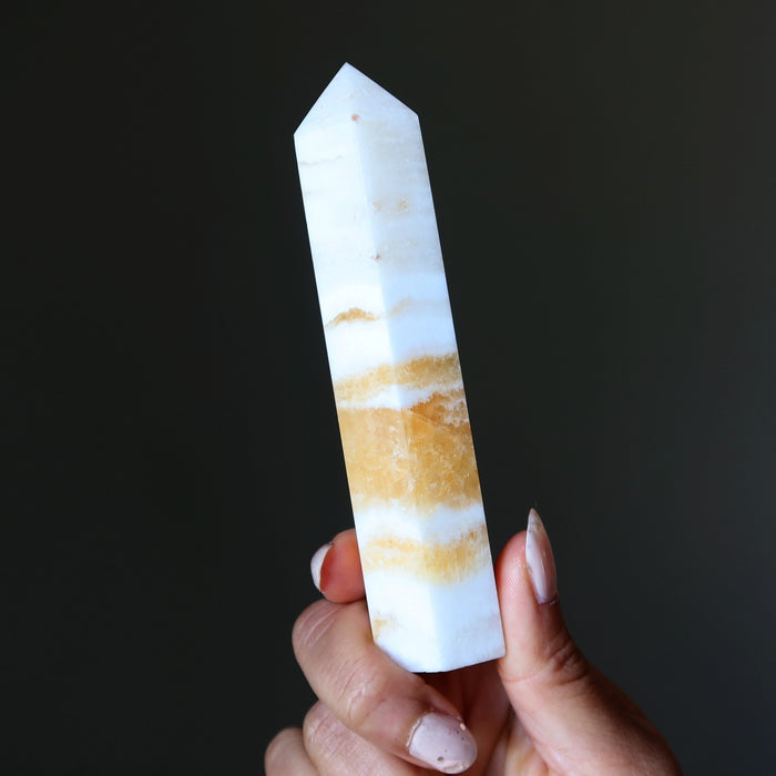 Hand holding a striped calcite crystal against a dark background
