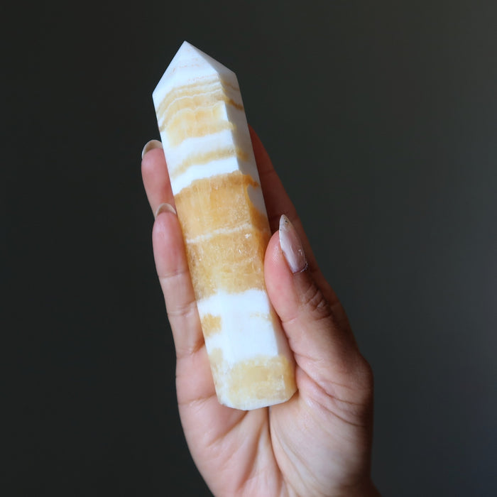 Hand holding a striped yellow calcite tower wand against a dark background