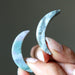 Hand holding two japer stone crescent moon shapes against a dark background