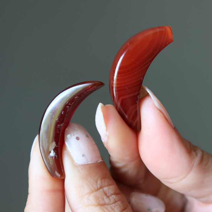 Two red carnelian stone carvings held between fingers against a gray background