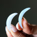 Two white agate crescent-shaped objects held between fingers against a dark background