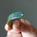 Hand holding a green jasper stone against a gray background
