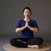Person sitting in a meditative pose with hands pressed together on a gray background