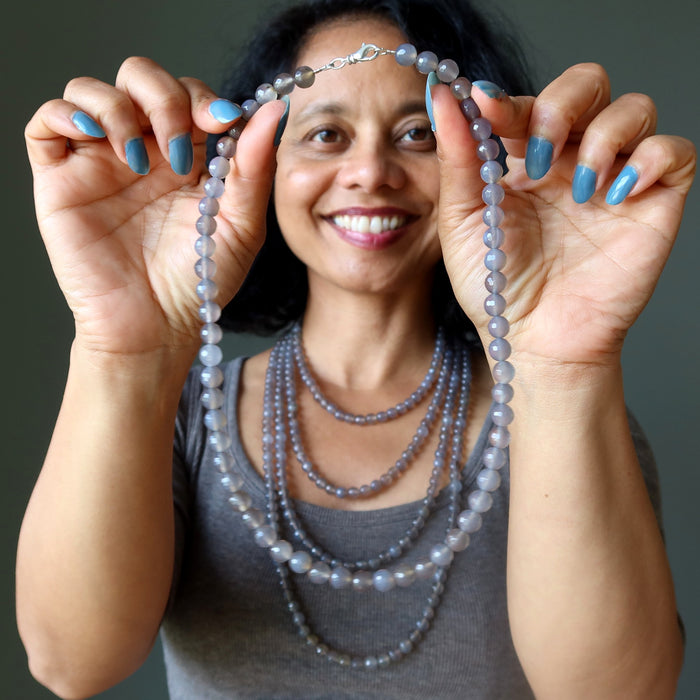 Woman holding a gray chalcedony beaded necklace against a neutral background