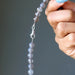 Hand holding a string of gray chalcedony beads against a gray background