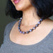 Woman wearing a beaded charoite necklace with a neutral background