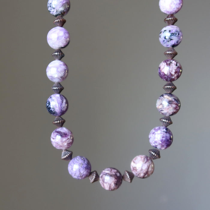 Necklace with purple charoite beads and silver accents on a neutral background