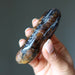 Hand holding a polished chiastolite stone with a dark and light banding pattern against a neutral background