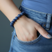Hand wearing a blue dumortierite beaded bracelet with denim jeans on a gray background