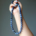 Hand holding a blue dumortierite beaded necklace against a gray background