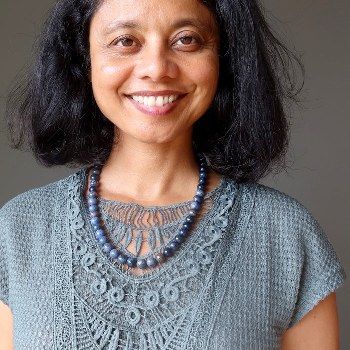 Woman wearing a gray lace top and blue dumortierite beaded necklace against a neutral background