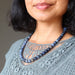 Woman wearing a blue dumortierite beaded necklace with a gray lace top against a neutral background