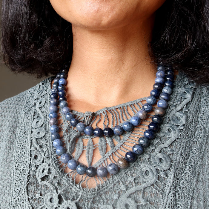 blue dumortierite beaded necklaces worn by a person against a gray lace garment.