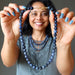 Woman holding a blue dumortierite beaded necklace in front of her face against a gray background