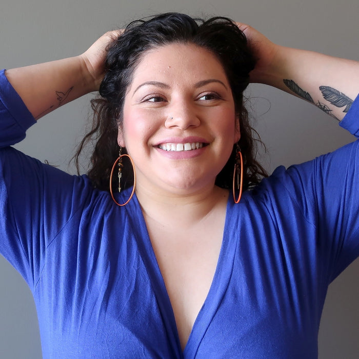 Woman wearing a blue top with orange hoop earrings against a neutral background