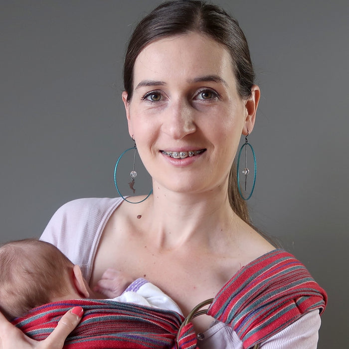 Woman holding a baby in a sling against a gray background