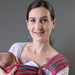 Woman holding a baby in a sling against a gray background