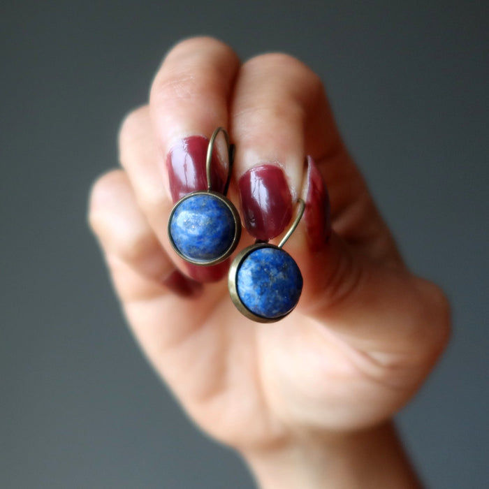 Hand holding a pair of blue stone earrings against a gray background