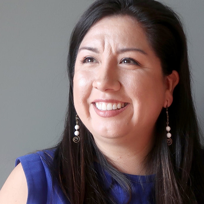 Woman with long dark hair wearing a blue top against a gray background