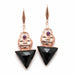 Black triangle earrings with rose gold accents held in a hand against a wooden background.