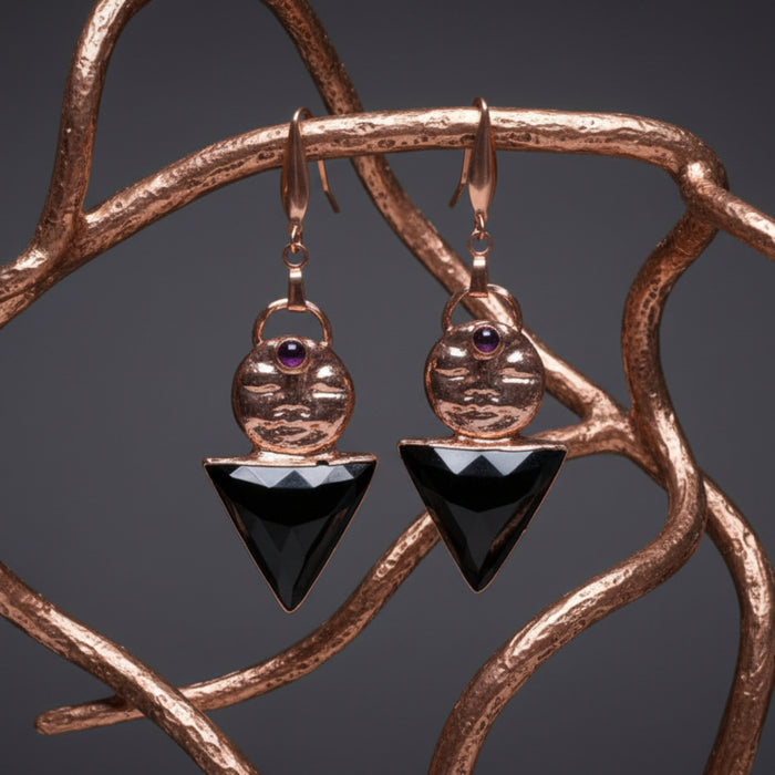 Rose gold earrings with black triangle charms held in a hand against a wooden surface.