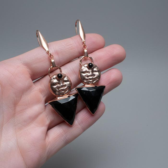 Rose gold and black earrings held in a hand with a natural background