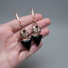 Rose gold and black earrings held in a hand with a natural background
