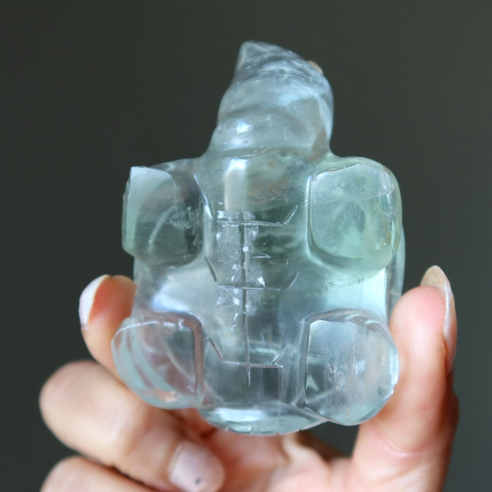 Clear green fluorite crystal sculpture  held in hands against a dark background