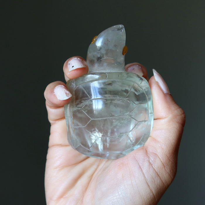 Clear green fluorite turtle held in a hand against a dark background