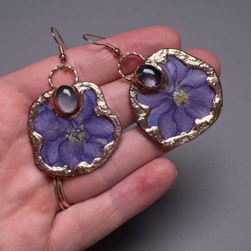 Earrings with purple floral design and gold accents held in a hand against a gray background