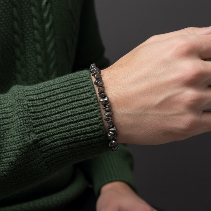 Person wearing a dark green sweater with a hematite bracelet on a dark background