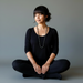 Woman sitting in a meditative pose on a plain background with hematite necklace