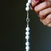 Hand holding a Howlite necklace with white beads against a dark background