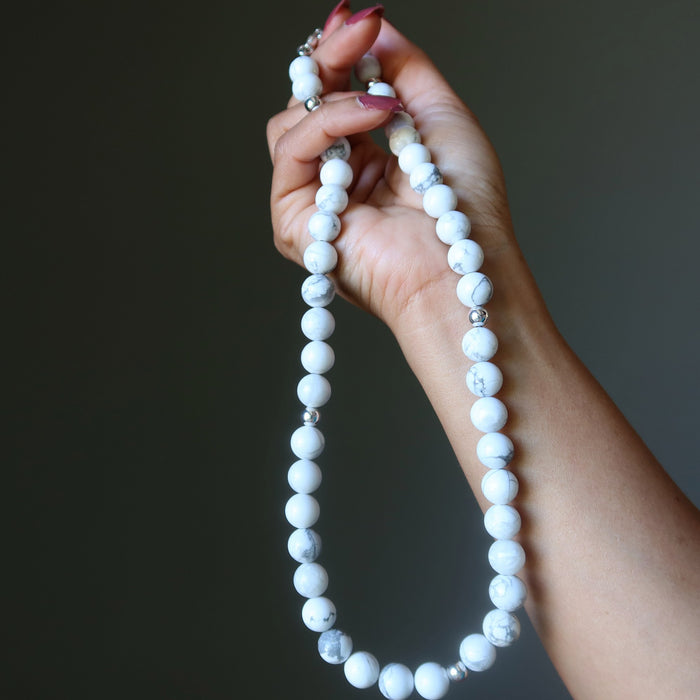 Hand holding a white beaded Howlite necklace against a dark background