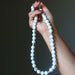 Hand holding a white beaded Howlite necklace against a dark background