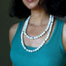 Woman wearing a teal tank top and white Howlite necklace against a dark background