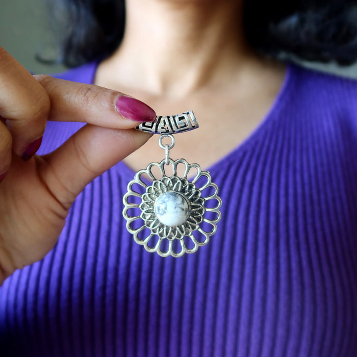 Silver floral Howlite pendant  held by a hand with purple nail polish against a blurred purple garment background