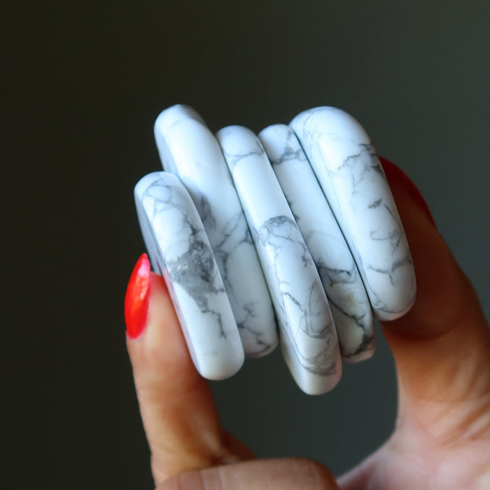 howlite slabs on a hand with red nail polish against a dark background