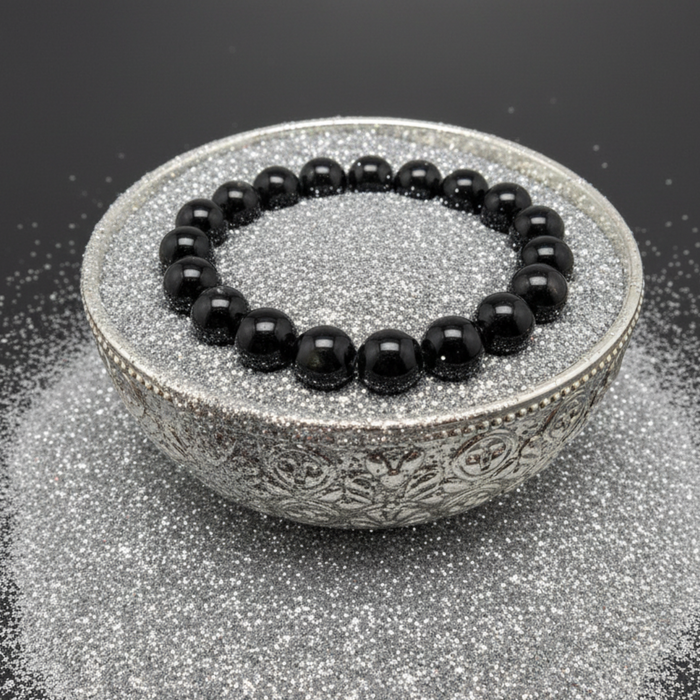 Black beaded hypersthene bracelet on a decorative silver bowl with a black background