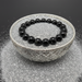 Black beaded hypersthene bracelet on a decorative silver bowl with a black background