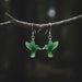 Green jade bird-shaped earrings on a wooden surface