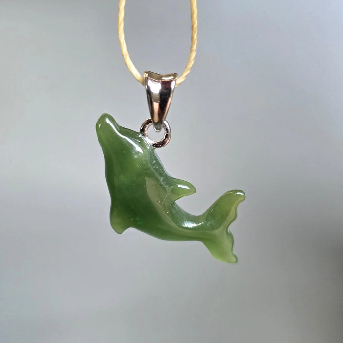 Green dolphin pendant on a gold chain against a gray background