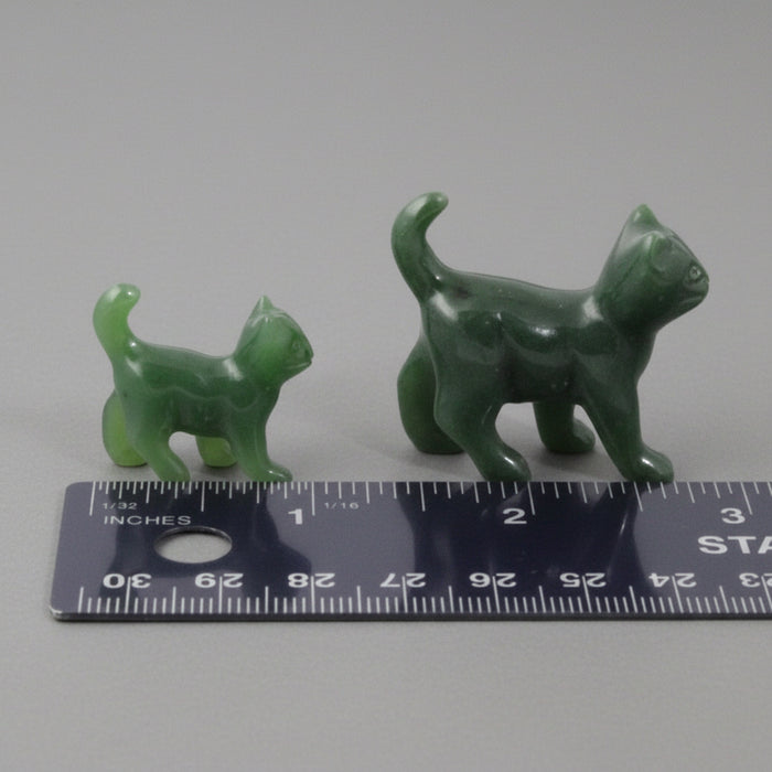 Two green jade cat figurines next to a ruler on a white background