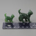 Two green jade cat figurines next to a ruler on a white background