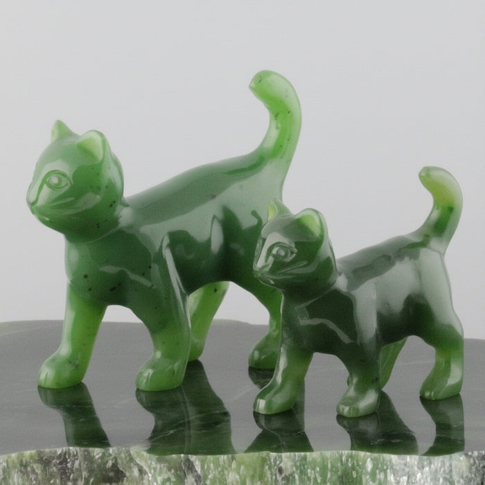 Two green jade cat figurines on a reflective surface with a white background