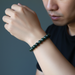 Person wearing a green jade beaded bracelet on a dark background
