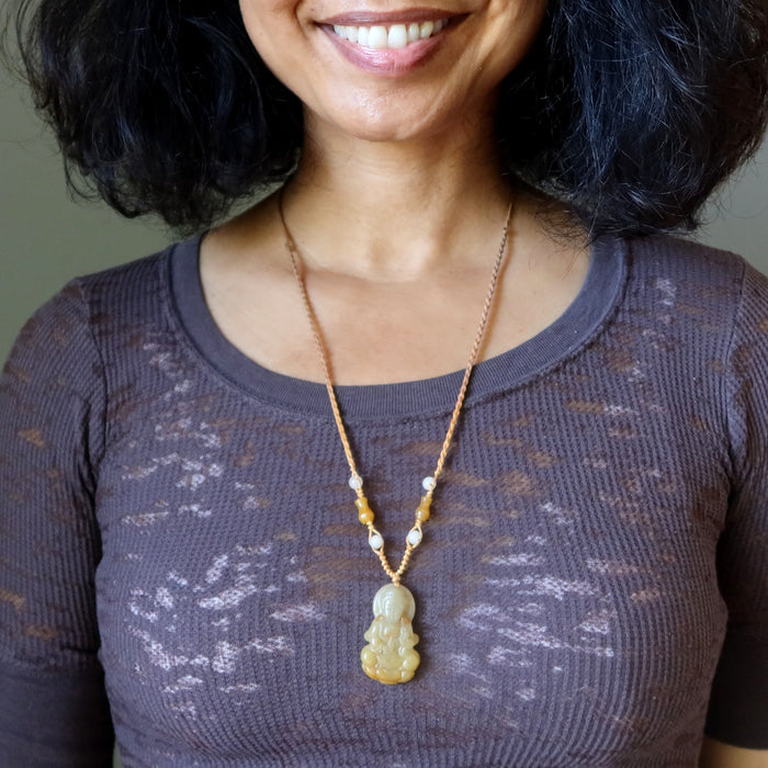 Woman wearing a Yellow Jade Kwan Yin Necklace with a pendant against a neutral background