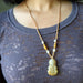 Yellow Jade Kwan Yin Necklace worn by a person against a gray background