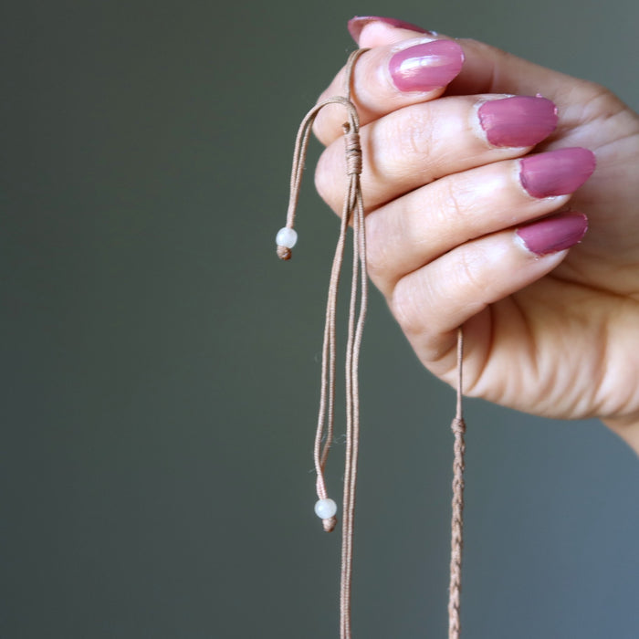 Hand holding a braided cord with small beads against a neutral background
